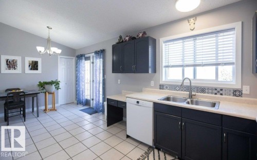 Kitchen featuring dark cabinetry, light countertops, dual basin sink, and white tile flooring - 10812 109 Street, Westlock, AB - Indoor Photo Showing Kitchen With Double Sink