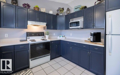 U-shaped kitchen featuring painted blue cabinetry, light countertops, and white tile flooring - 10812 109 Street, Westlock, AB - Indoor Photo Showing Kitchen