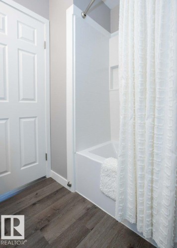 Bathroom featuring a white tub-shower combination with an integrated soap niche, dark wood-finish flooring, and a six-panel interior door - 10812 109 Street, Westlock, AB - Indoor