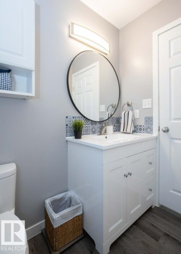 Contemporary vanity with white shaker-style cabinetry, a white countertop, and a circular black-framed mirror - 10812 109 Street, Westlock, AB - Indoor Photo Showing Bathroom