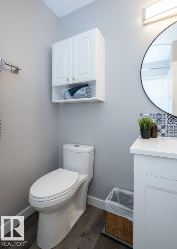 Full bathroom featuring a white vanity with a solid surface countertop, a round wall-mounted mirror, and a white toilet - 10812 109 Street, Westlock, AB - Indoor Photo Showing Bathroom