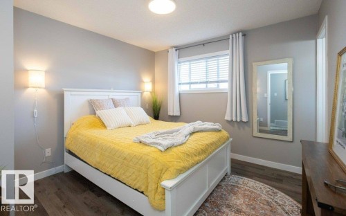Bedroom featuring wood-finish flooring, a window with horizontal blinds, and two wall-mounted sconces - 10812 109 Street, Westlock, AB - Indoor Photo Showing Bedroom