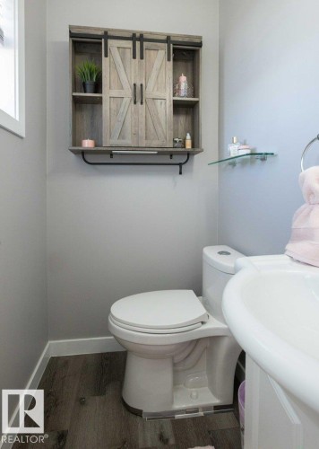 Powder room featuring a wood-finish wall cabinet with barn-door style sliders, a white pedestal sink, and wood-finish flooring - 10812 109 Street, Westlock, AB - Indoor Photo Showing Bathroom