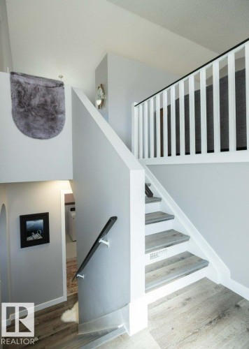 Multi-level interior featuring wood-finish flooring, a white spindle railing with a dark top rail, and a coordinating dark wall-mounted handrail - 10812 109 Street, Westlock, AB - Indoor Photo Showing Other Room