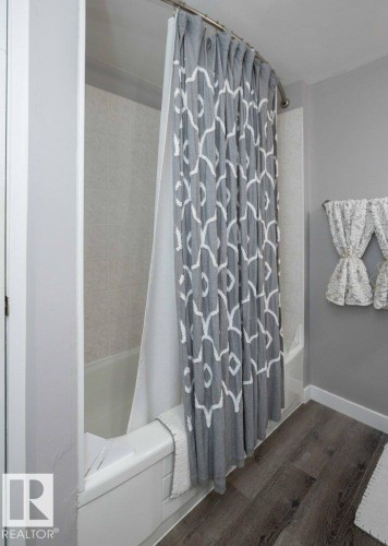 Bathtub with tiled surround and wood-finish flooring - 10812 109 Street, Westlock, AB - Indoor Photo Showing Bathroom
