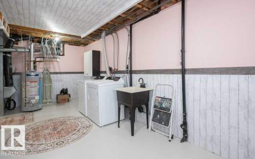 Laundry area featuring a utility sink with a black faucet, light pink walls, and white wood-finish wainscoting - 10812 109 Street, Westlock, AB - Indoor Photo Showing Laundry Room