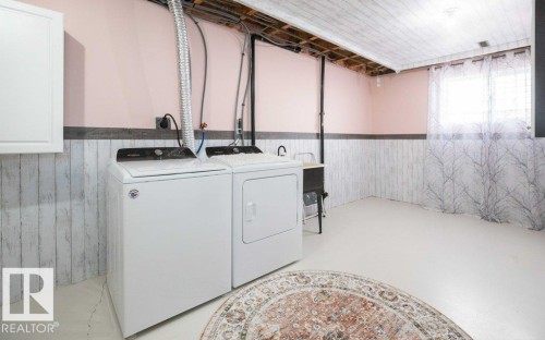 Dedicated laundry area featuring a washer and dryer, utility sink, white wood-finish wainscoting, and exposed ceiling joists - 10812 109 Street, Westlock, AB - Indoor Photo Showing Laundry Room