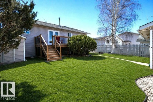 Expansive rear yard featuring a wooden deck with railing and stairs, a separate storage shed, partial picket fencing, and a mature tree - 10812 109 Street, Westlock, AB - Outdoor