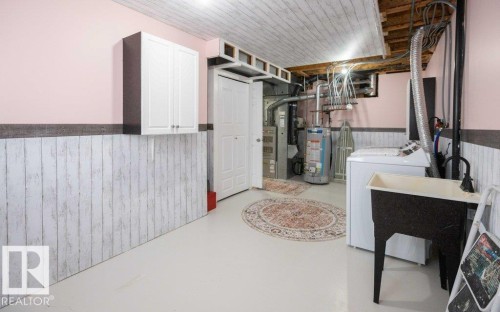 Utility room with white paneling and pink walls, featuring white painted flooring and overhead cabinetry - 10812 109 Street, Westlock, AB - Indoor Photo Showing Laundry Room