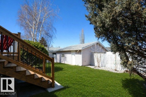 Backyard featuring a wooden deck with black metal balusters, a manicured lawn, an outbuilding with vinyl siding, and a white picket fence - 10812 109 Street, Westlock, AB - Outdoor