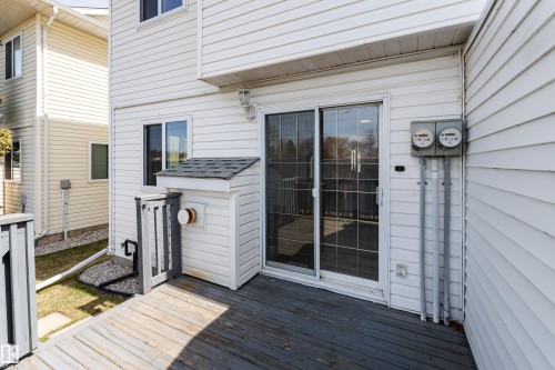 Private deck area featuring white vinyl siding, a sliding glass door, a window with dark trim, and a white utility enclosure with a shingled roof - #63 1033 Youville Dr W Nw, Edmonton, AB - Outdoor With Deck Patio Veranda With Exterior