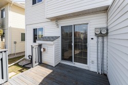 Private deck area featuring white vinyl siding, a sliding glass door, a window with dark trim, and a white utility enclosure with a shingled roof - 