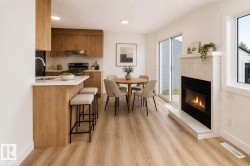 Open-concept living space featuring a tiled fireplace with hearth, wood-finish flooring, and a kitchen with wood cabinetry and light countertops - 