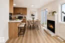 Open-concept living space featuring a tiled fireplace with hearth, wood-finish flooring, and a kitchen with wood cabinetry and light countertops - #63 1033 Youville Dr W Nw, Edmonton, AB  - Indoor With Fireplace 
