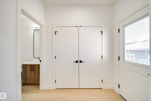 Entryway featuring light wood-finish flooring, white doors with matte black hardware, and a partial glass door with integrated blinds - 92 Blackbird Bend E, Fort Saskatchewan, AB - Indoor Photo Showing Other Room