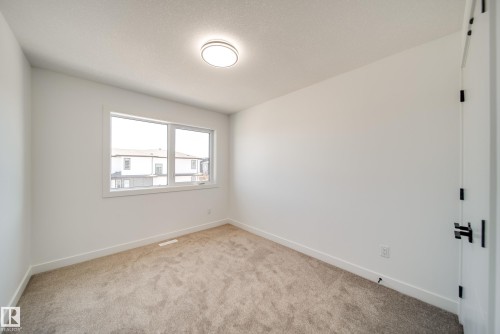 Bright room featuring a large window, neutral carpeting, white trim, a modern ceiling light fixture, and a white door with matte black hardware - 92 Blackbird Bend E, Fort Saskatchewan, AB - Indoor Photo Showing Other Room