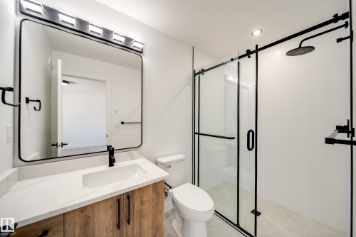 Contemporary bathroom featuring a black-framed mirror, wood-finish vanity with a white countertop, and a glass-enclosed shower with black hardware - 92 Blackbird Bend E, Fort Saskatchewan, AB - Indoor Photo Showing Bathroom