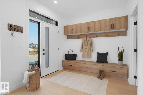Entryway featuring a built-in wood-finish bench with drawers, coordinating overhead cabinetry, a wall-mounted coat rack, and light wood-finish flooring - 92 Blackbird Bend E, Fort Saskatchewan, AB - Indoor Photo Showing Other Room