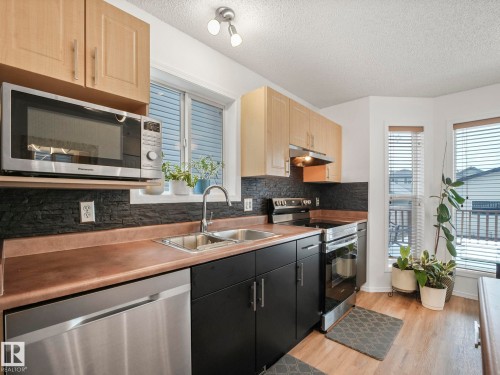 The kitchen features light wood cabinetry, dark countertops, and a black brick-patterned backsplash - 21360 88 Avenue, Edmonton, AB - Indoor Photo Showing Kitchen With Double Sink