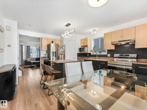 Contemporary kitchen featuring light wood cabinetry, dark backsplash, stainless steel appliances, and a central island with bar seating - 21360 88 Avenue, Edmonton, AB - Indoor