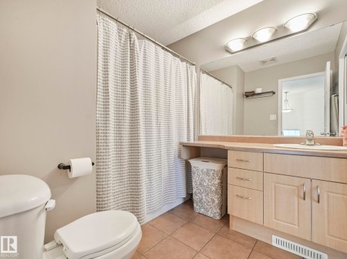 Bathroom with a neutral color palette, featuring a toilet, a shower with a patterned curtain, a vanity with a light wood finish, a countertop, and a large mirror with overhead lighting - 21360 88 Avenue, Edmonton, AB - Indoor Photo Showing Bathroom