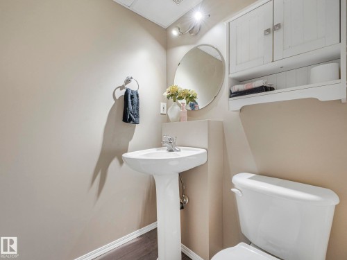This powder room features a pedestal sink with a chrome faucet, an oval mirror, and a wall-mounted white storage cabinet - 21360 88 Avenue, Edmonton, AB - Indoor Photo Showing Bathroom