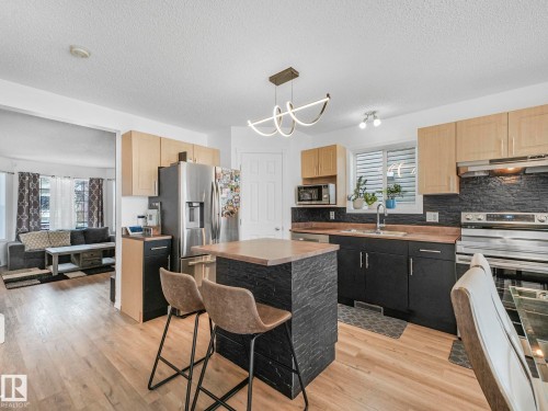 This kitchen features light-toned wood flooring, a central island with a wood countertop, and a modern light fixture - 21360 88 Avenue, Edmonton, AB - Indoor Photo Showing Kitchen