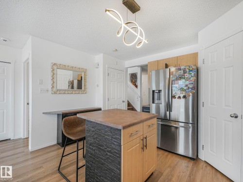 The kitchen features a central island with a countertop, wood cabinetry, and a stainless steel refrigerator - 21360 88 Avenue, Edmonton, AB - Indoor