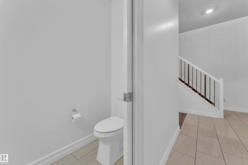 White toilet with a chrome toilet paper holder and tile flooring - 3235 13 Avenue, Edmonton, AB - Indoor Photo Showing Bathroom
