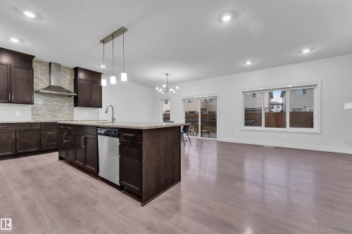 Modern kitchen featuring dark wood cabinetry, a central island with a sink and pendant lighting, and stainless steel appliances - 3235 13 Avenue, Edmonton, AB - Indoor Photo Showing Kitchen With Upgraded Kitchen