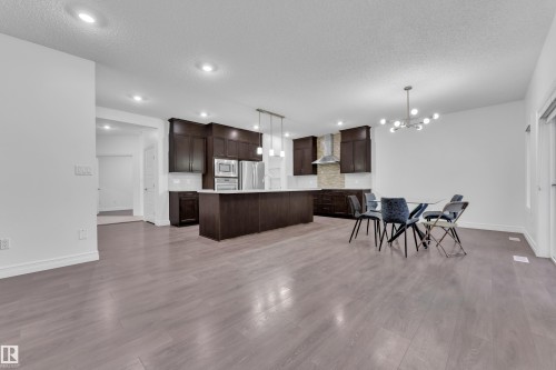 Expansive kitchen featuring dark wood cabinetry, stainless steel appliances, a large island with pendant lighting, and a stone-tiled backsplash - 3235 13 Avenue, Edmonton, AB - Indoor