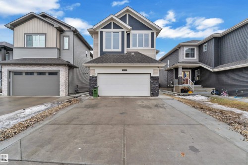 Contemporary two-story home featuring a dark blue and light tan siding exterior, a white garage door, and a stone facade accent - 3235 13 Avenue, Edmonton, AB - Outdoor With Facade