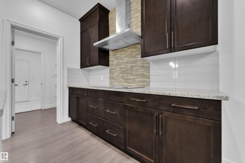 Kitchen featuring dark wood cabinetry, light-toned countertop, a range hood, and a decorative tile backsplash - 3235 13 Avenue, Edmonton, AB - Indoor