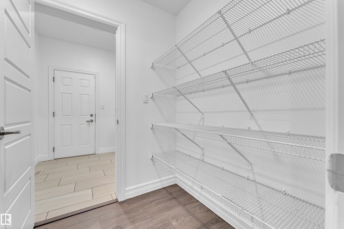 Utility area featuring white wire shelving, a contrasting wood-finish floor, and a white paneled door with brushed nickel hardware - 3235 13 Avenue, Edmonton, AB - Indoor With Storage