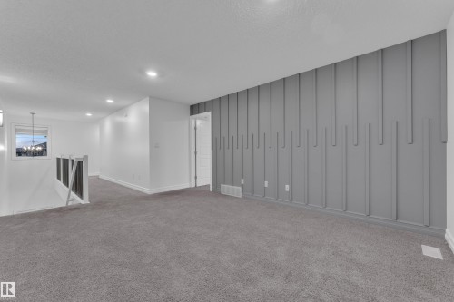 Open concept living space featuring a textured accent wall, plush carpeting, recessed lighting, and a white painted banister - 3235 13 Avenue, Edmonton, AB - Indoor Photo Showing Other Room