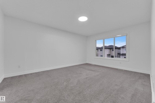 Spacious interior room featuring light gray carpeting, crisp white walls, and a large three-pane window - 3235 13 Avenue, Edmonton, AB - Indoor Photo Showing Other Room
