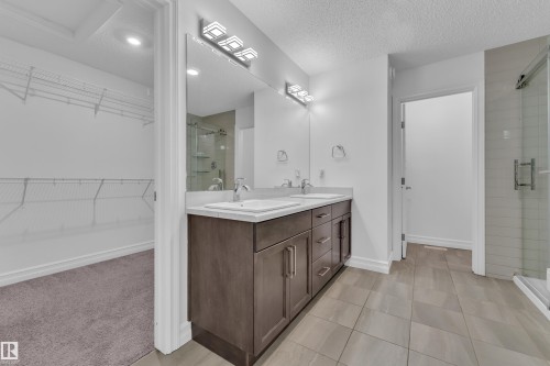 Bathroom featuring a dual vanity with a light-toned countertop, rectangular sinks, and wood-finish cabinetry - 3235 13 Avenue, Edmonton, AB - Indoor Photo Showing Bathroom