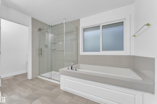 Bathroom featuring an integrated soaking tub, a separate glass-enclosed shower, a frosted window, and large format floor tiling - 3235 13 Avenue, Edmonton, AB - Indoor Photo Showing Bathroom