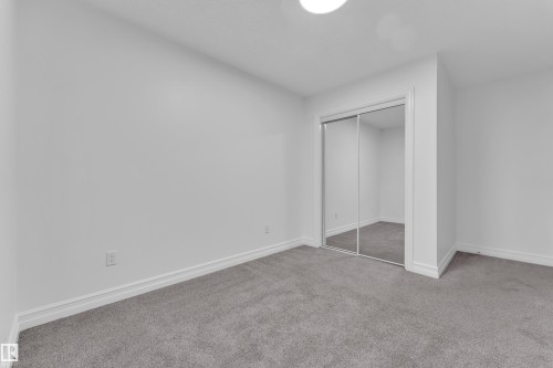Bedroom featuring a mirrored closet, neutral gray carpeting, white baseboards, and a flush-mount ceiling light - 3235 13 Avenue, Edmonton, AB - Indoor Photo Showing Other Room