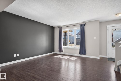 Spacious living area featuring wood-finish flooring, a prominent accent wall, and a large window with white trim - 332 Nelson Drive, Spruce Grove, AB - Indoor