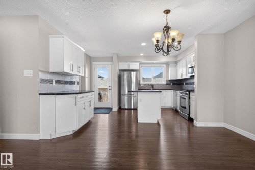 Open concept kitchen featuring white cabinetry, dark countertops, a tile backsplash, stainless steel appliances, and a central island with a breakfast bar - 332 Nelson Drive, Spruce Grove, AB - Indoor Photo Showing Kitchen
