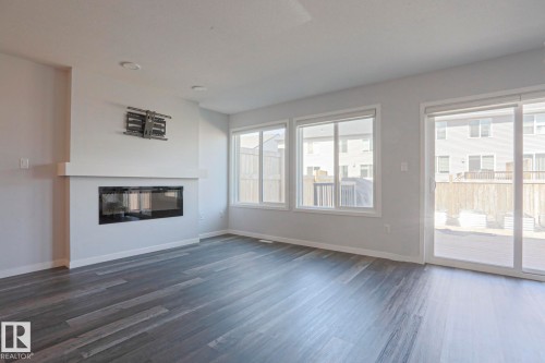 Spacious room featuring wood-finish flooring, a contemporary fireplace with mantel, recessed ceiling lighting, and multiple windows providing natural illumination - 4314 Cooke Lane, Edmonton, AB - Indoor Photo Showing Living Room With Fireplace