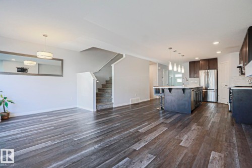 Open-concept living space featuring wood-finish flooring, a modern kitchen island with pendant lighting, dark wood cabinetry, stainless steel appliances, and a carpeted staircase - 4314 Cooke Lane, Edmonton, AB - Indoor Photo Showing Kitchen With Stainless Steel Kitchen With Upgraded Kitchen