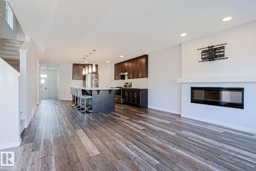 Open-concept living space featuring wood-finish flooring, a contemporary linear fireplace with a white mantel, and recessed ceiling lighting - 4314 Cooke Lane, Edmonton, AB - Indoor Photo Showing Living Room With Fireplace