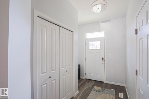 Entryway featuring wood-finish flooring, a white front door with transom window, a flush mount ceiling light, and bi-fold closet doors - 4314 Cooke Lane, Edmonton, AB - Indoor Photo Showing Other Room