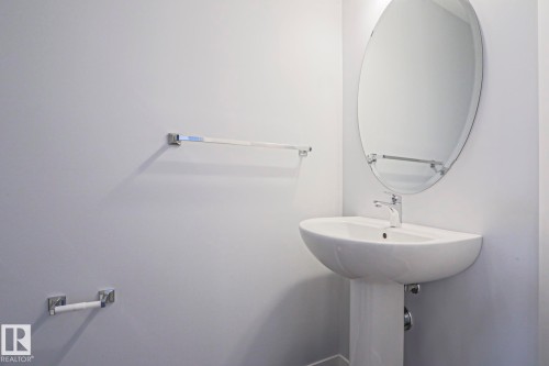 Pedestal sink with chrome faucet, complemented by an oval-shaped mirror, chrome towel bar, and chrome toilet paper holder - 4314 Cooke Lane, Edmonton, AB - Indoor Photo Showing Bathroom