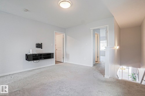 Carpeted room with light gray walls, featuring a flush-mount ceiling light and a wall-mounted floating media console - 4314 Cooke Lane, Edmonton, AB - Indoor