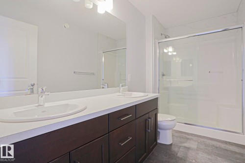 Contemporary bathroom featuring a dark wood-finish double vanity with dual undermount sinks, a wide mirror, a glass-enclosed shower, and grey tile-look flooring - 4314 Cooke Lane, Edmonton, AB - Indoor Photo Showing Bathroom