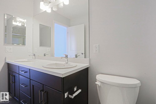 Bathroom featuring a dual-sink vanity with dark wood-finish cabinetry, white countertop, and integrated sinks - 4314 Cooke Lane, Edmonton, AB - Indoor Photo Showing Bathroom