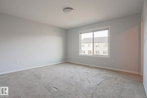 Spacious room featuring neutral gray carpeting and walls, a large window with white trim, and a flush-mount ceiling light fixture - 4314 Cooke Lane, Edmonton, AB - Indoor Photo Showing Other Room